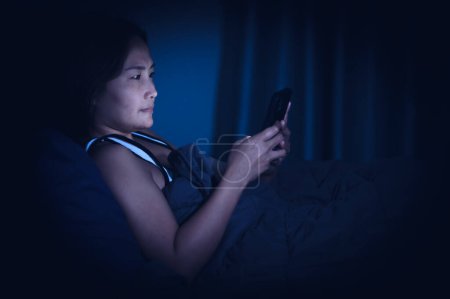 Foto de Mujer asiática jugar smartphone en la cama por la noche, Tailandia personas - Imagen libre de derechos