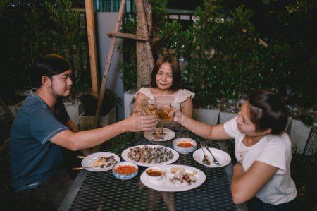 Foto de Grupo de personas asiáticas cenando fiesta en el jardín de la casa de vacaciones, Fiesta de verano por la noche jardín con amigos - Imagen libre de derechos