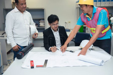 Photo for Three asian engineers looking paper plan of the building,Discuss about the problems and solutions of the construction in the office,Customer complaints engineers about green building send no on schedule - Royalty Free Image