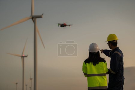 Photo for Two engineers working and holding the report at wind turbine farm Power Generator Station on mountain,Thailand people,Technician man and woman discuss about wor - Royalty Free Image