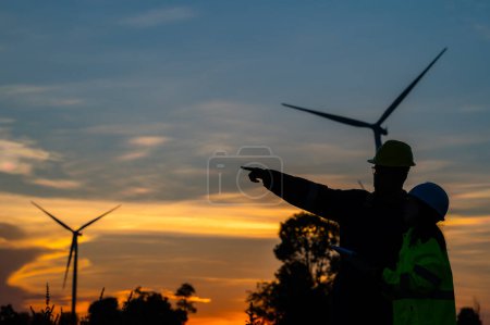 Photo for Two engineers working and holding the report at wind turbine farm Power Generator Station on mountain,Thailand people,Technician man and woman discuss about work - Royalty Free Image