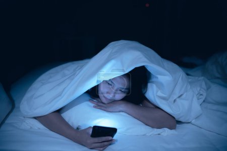 Foto de Mujer asiática jugando en el teléfono inteligente en la cama por la noche, Tailandia personas, adicto a las redes sociales - Imagen libre de derechos
