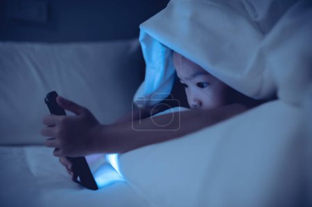 Photo for Asian kid playing game on smartphone in the bed at night,The girl Addict social media - Royalty Free Image