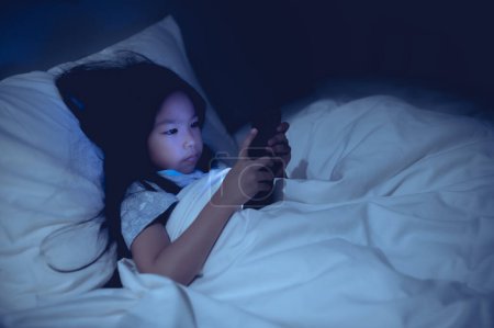 Foto de Asian kid playing game on smartphone in the bed at night,The girl Addict social media - Imagen libre de derechos