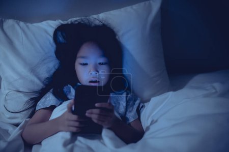 Foto de Asian kid playing game on smartphone in the bed at night,The girl Addict social media - Imagen libre de derechos