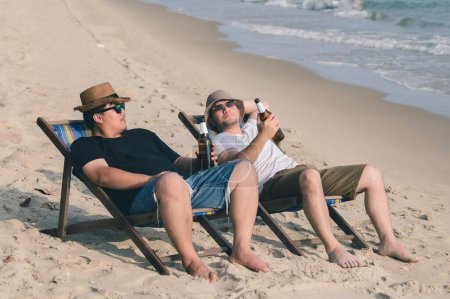 Foto de Dos hombres beben cerveza en la playa, hora de verano con un amigo en el mar, tiempo de relax, pareja amor de lgbt gay - Imagen libre de derechos