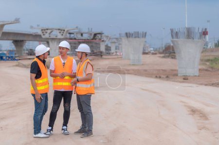Foto de Grupo de ingenieros asiáticos discuten sobre el trabajo en el sitio de la construcción en construcción, El equipo del contratista discute el diseño de la estructura, Tres trabajadores están trabajando fuera. - Imagen libre de derechos