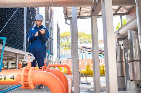 Téléchargez les photos : Jeune ingénieur travaillant dans une grande usine, technicien en uniforme de protection et avec contrôle de la température du casque dans les tuyaux - en image libre de droit