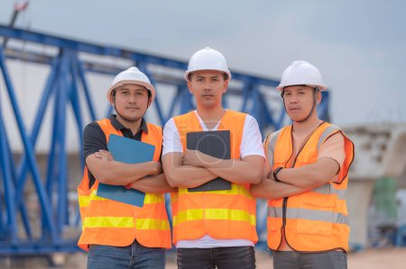 Téléchargez les photos : Groupe d'ingénieurs asiatiques discuter des travaux sur le site du bâtiment en construction, L'équipe de l'entrepreneur discute de la conception de la structure, Trois travailleurs travaillent à l'extérieur. - en image libre de droit