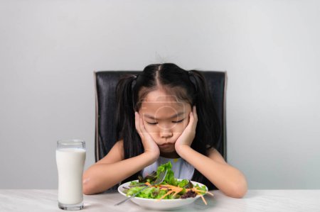 Foto de Pequeña chica linda asiática se niega a comer verduras saludables.Nutrition y hábitos alimenticios saludables para los niños concept.Children no les gusta comer verduras. - Imagen libre de derechos