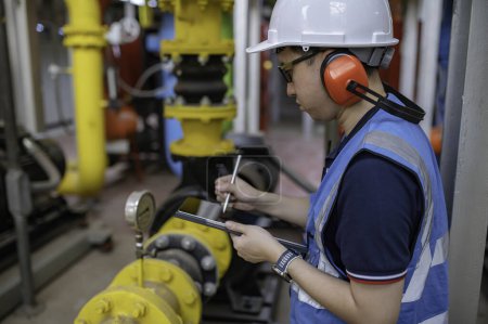 Foto de Técnico de mantenimiento en una planta de calefacción, trabajadores petroquímicos supervisan la operación de gasoductos y oleoductos en la fábrica, ingenieros ponen protector auditivo en la habitación con muchas tuberías - Imagen libre de derechos