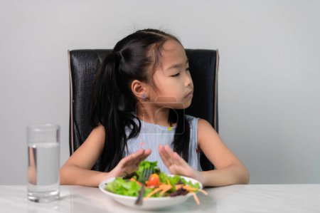 Téléchargez les photos : Petite fille mignonne asiatique refuse de manger des légumes sains.Nutrition & saines habitudes alimentaires pour les enfants concept.Children n'aiment pas manger des légumes. - en image libre de droit