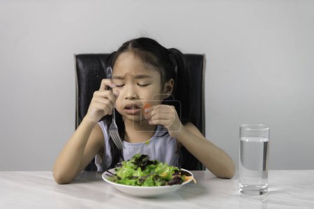 Photo for Little asian cute girl refuses to eat healthy vegetables.Nutrition & healthy eating habits for kids concept.Children do not like to eat vegetables. - Royalty Free Image