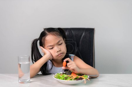 Photo for Little asian cute girl refuses to eat healthy vegetables.Nutrition & healthy eating habits for kids concept.Children do not like to eat vegetables. - Royalty Free Image
