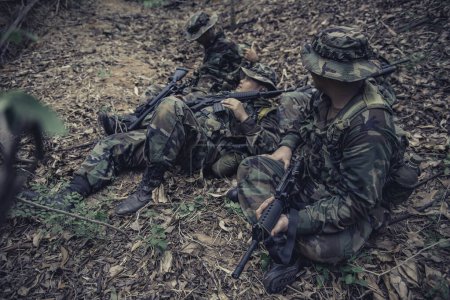 Téléchargez les photos : Équipe de soldat de l'armée avec mitrailleuse se déplaçant dans la forêt, soldat de la milice thaïlandaise en uniformes de combat dans le bois, Errez la patrouille en pente dans la forêt tropicale. - en image libre de droit
