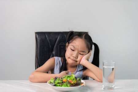 Foto de Pequeña chica linda asiática se niega a comer verduras saludables.Nutrition y hábitos alimenticios saludables para los niños concept.Children no les gusta comer verduras. - Imagen libre de derechos