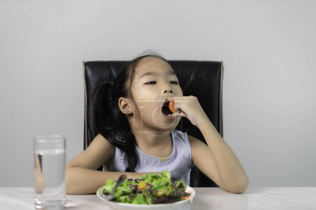 Foto de Pequeña chica linda asiática para comer verduras saludables.Nutrition y hábitos alimenticios saludables para los niños concept.Children feliz y le gusta comer verduras. - Imagen libre de derechos