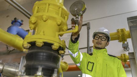 Téléchargez les photos : Ingénieur asiatique portant des lunettes travaillant dans la chaufferie, vérification de la maintenance des données techniques de l'équipement du système de chauffage. Thaïlande peuple - en image libre de droit