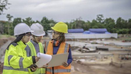 Photo for Young and senior Engineers discuss about work of large building under construction. Three people working on site of under construction - Royalty Free Image