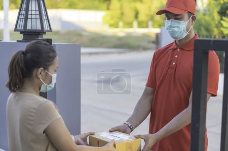 Téléchargez les photos : Asian Delivery un masque protecteur d'usure en uniforme rouge. Nourriture en ligne et concept de livraison de produits. Nouvelle normale dans covid-19 - en image libre de droit