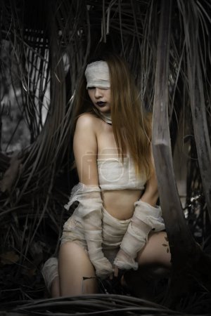 Téléchargez les photos : Portrait de belle femme asiatique sexy porter costume momie dans la forêt. Scène de film d'horreur. Affiche Halloween - en image libre de droit