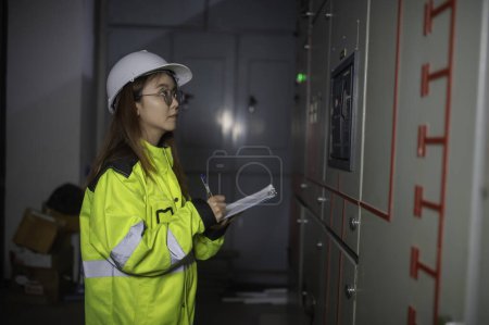 Téléchargez les photos : Ingénieur électrique asiatique tenant presse-papiers pour vérifier et surveiller le système électrique dans la salle de contrôle. Technicien thailand personnes travaillant - en image libre de droit