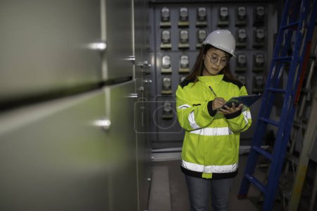 Téléchargez les photos : Ingénieur électrique asiatique tenant presse-papiers pour vérifier et surveiller le système électrique dans la salle de contrôle. Technicien thailand personnes travaillant - en image libre de droit
