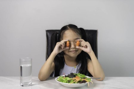 Téléchargez les photos : Petite fille mignonne asiatique pour manger des légumes sains. Nutrition et saines habitudes alimentaires pour les enfants concept. Enfant heureux et aime manger des légumes. - en image libre de droit