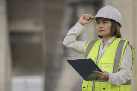 Photo for An Asian female engineer works at a motorway bridge construction site. Civil worker inspecting work on crossing construction - Royalty Free Image