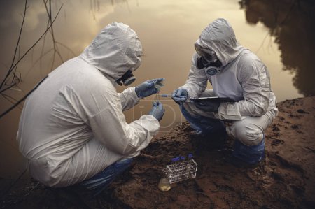 Foto de Científicos o biólogos que usan uniformes protectores trabajando juntos en el análisis del agua. Ingenieros ambientales inspeccionan la calidad del agua en una zona peligrosa - Imagen libre de derechos