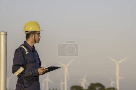 Téléchargez les photos : Asian Man ingénieur travaillant et tenant le rapport au parc d'éoliennes Power Generator Station sur la montagne. Les Thaïlandais. Technicien homme sur le lieu de travail - en image libre de droit
