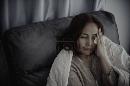 Foto de Mujer asiática enferma sentarse en el sofá quedarse en casa. La mujer se sentía mal, quería recostarse y descansar, fiebre alta - Imagen libre de derechos