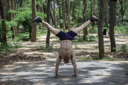 Photo for Handsome man exercises by hanging on a bar outdoor. Asian man trains for sporting events - Royalty Free Image