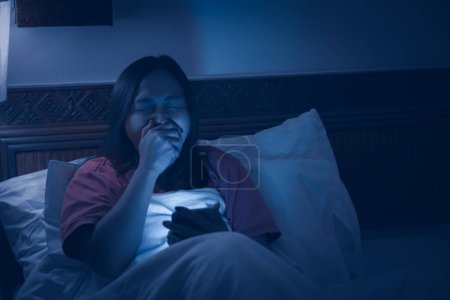 Téléchargez les photos : Femme asiatique jouant jeu sur smartphone dans le lit la nuit. Les Thaïlandais. Accro aux médias sociaux - en image libre de droit
