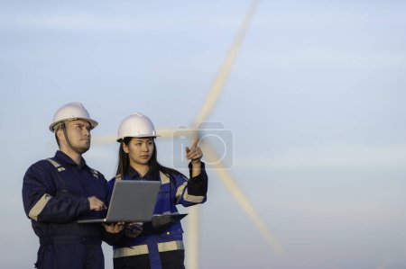Photo for Two engineers working and holding the report at wind turbine farm Power Generator Station on mountain. Thailand people. Technician man and woman discuss about work - Royalty Free Image