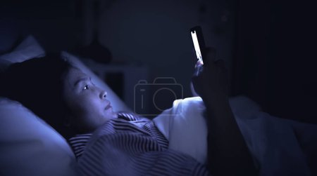 Foto de Mujer asiática jugando en el teléfono inteligente en la cama por la noche. Tailandia gente. Redes sociales adictas - Imagen libre de derechos