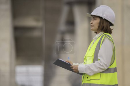 Téléchargez les photos : Une ingénieure asiatique travaille sur un chantier de construction de ponts autoroutiers. Travailleur civil inspectant les travaux de construction de passages à niveau - en image libre de droit