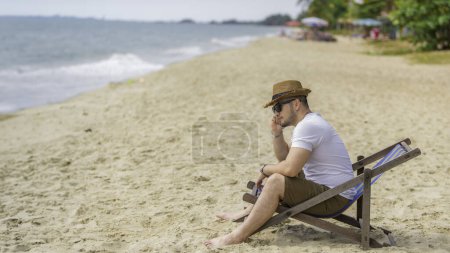 Téléchargez les photos : Asiatique homme assis chaise sur la plage de la mer. Détendez-vous en été - en image libre de droit