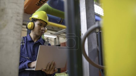 Photo for Maintenance technician at a heating plant. Petrochemical worker supervise the operation of gas and oil pipelines in the factory. Engineer put hearing protector At room with many pipes - Royalty Free Image