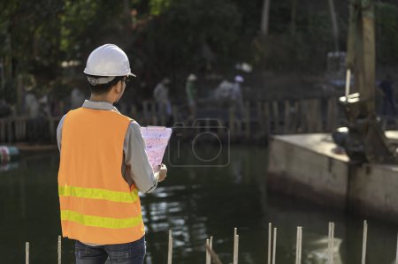 Photo for Construction engineer working on a bridge construction site over a river. Civil engineer supervising work. Foreman inspects work at a construction site - Royalty Free Image
