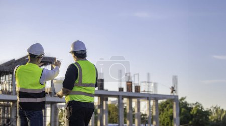 Photo for Two Asian engineers working at site of a large building project. Thailand people. Work overtime at construction site. Team of engineers discus at site - Royalty Free Image