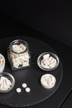 Foto de Complementos nutricionales en frascos sobre un escritorio negro sobre un fondo negro. Vitaminas y minerales para mejorar el nivel de vida. - Imagen libre de derechos