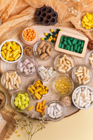 Große Menge verschiedener Nahrungsergänzungsmittel, Pillen, Vitamine, Mineralien, Tabletten und Kapseln in kleinen Gläsern von oben auf einem Holztisch auf beigem Hintergrund im rustikalen Stil. Gesunder Lebensstil.