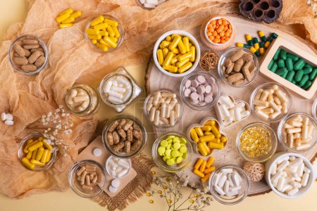 Grande quantité de divers compléments alimentaires pilules, vitamines, minéraux, comprimés et capsules dans de petits pots d'en haut sur un bureau en bois sur fond beige dans un style rustique. Mode de vie sain.