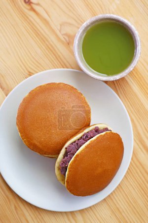 Assiette de Dorayaki délicieux avec une tasse de thé vert Matcha chaud servi sur une table en bois