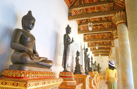 Foto de Visitor Impressed by a Row of Ancient Buddha Images Enshrined at the Cloister of The Marble Temple in Bangkok, Thailand - Imagen libre de derechos