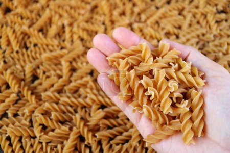 Photo for Heap of Dried Whole Wheat Fusilli Pasta in Hand with Blurry Pasta in Background - Royalty Free Image
