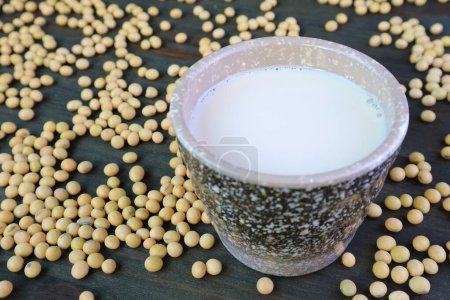 Foto de Primer plano de una taza de leche de soja con un montón de soja cruda esparcida - Imagen libre de derechos