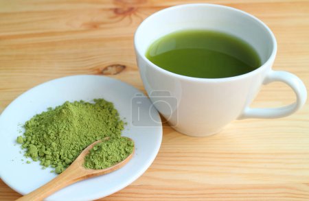 Foto de Taza de té verde matcha caliente con una placa de té matcha en polvo sobre mesa de madera - Imagen libre de derechos