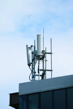 Téléchargez les photos : Antennes de téléphone portable sur le toit avec avion volant sur ciel nuageux - en image libre de droit